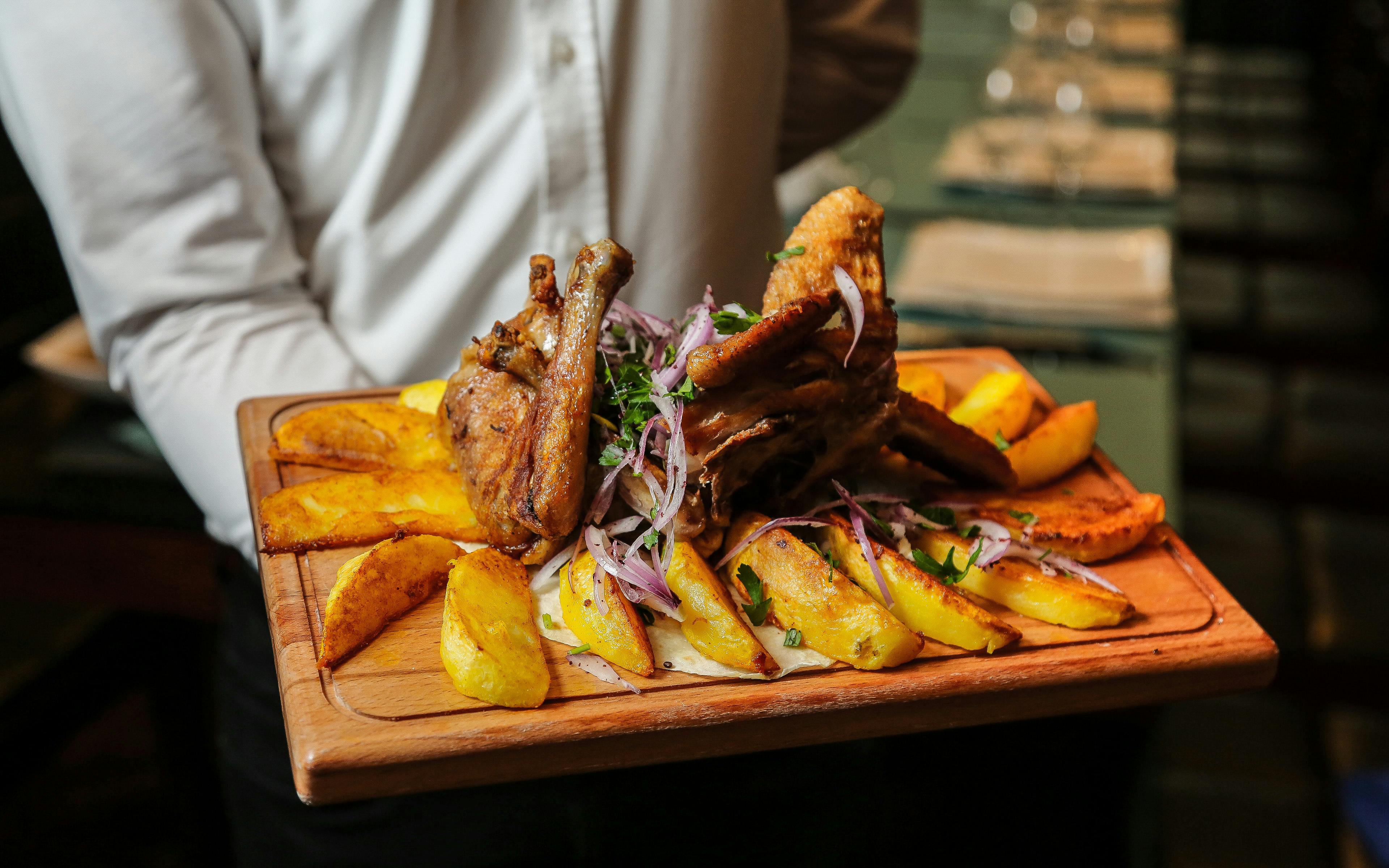 A wooden tray holding a meat-based dish, surrounded by wedges of crispy potatoes.
