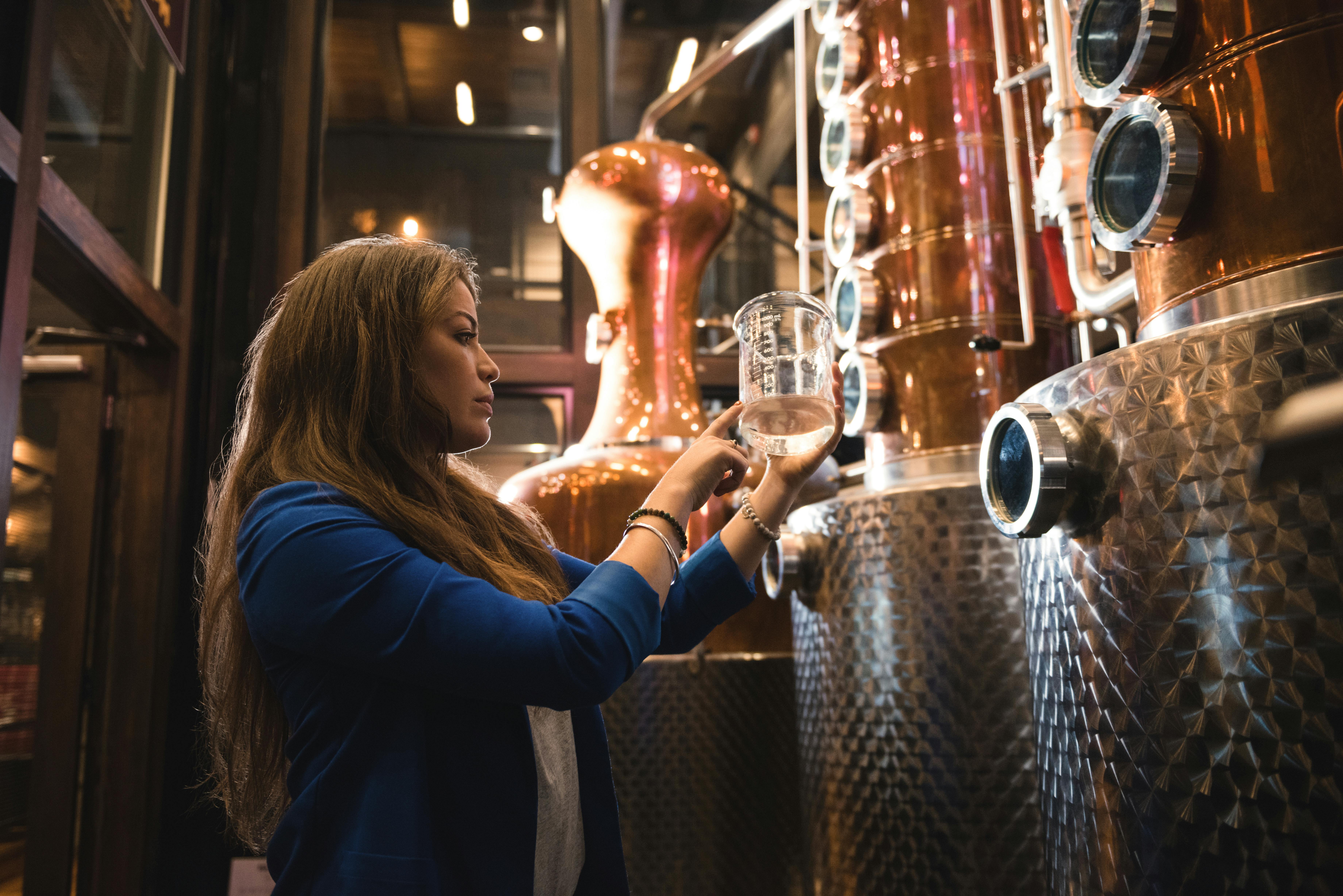 A woman inside a brewery, closely inspecting the brewing equipment during a tour.