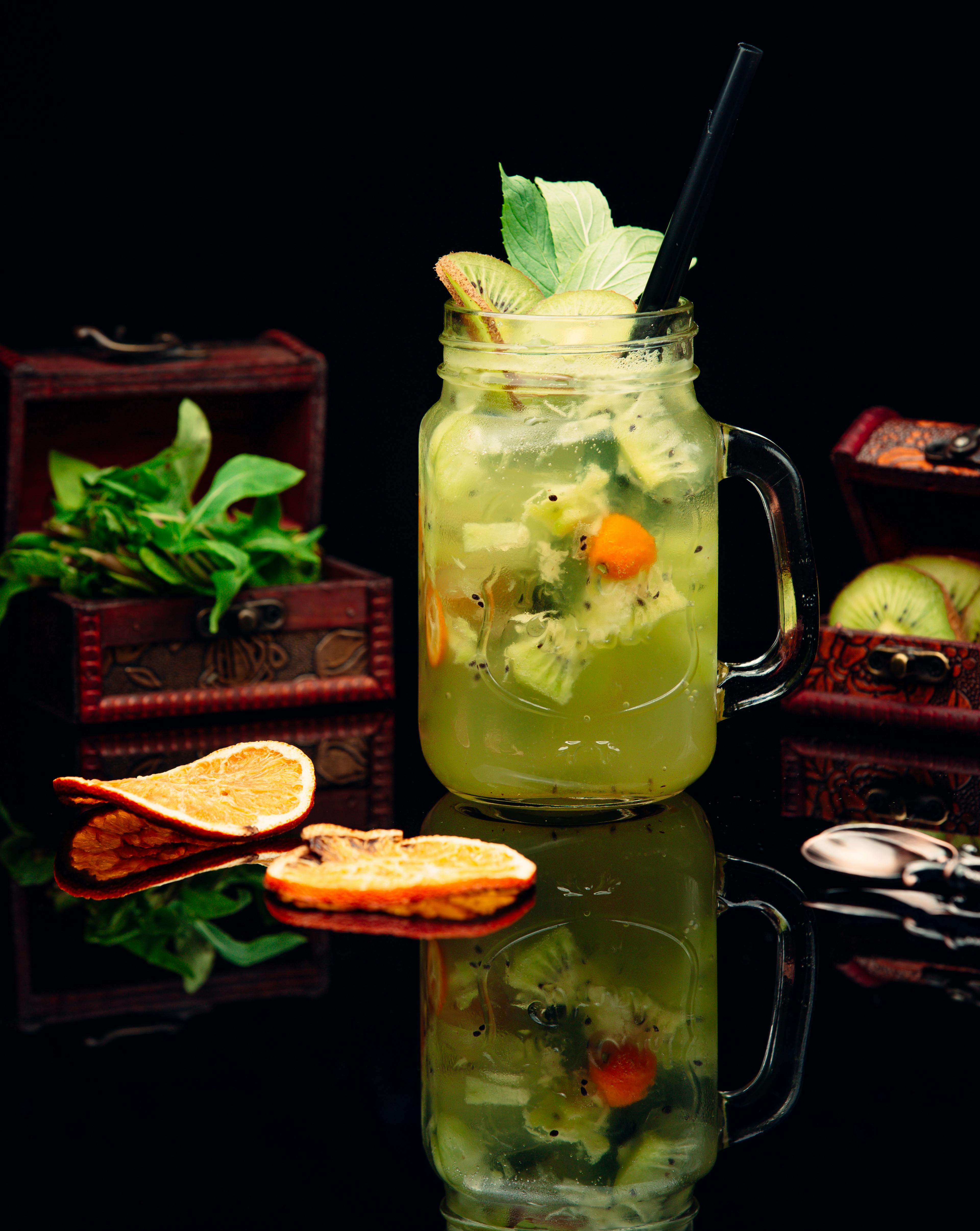 A glass of light green cocktail, garnished with a variety of mixed fruits.