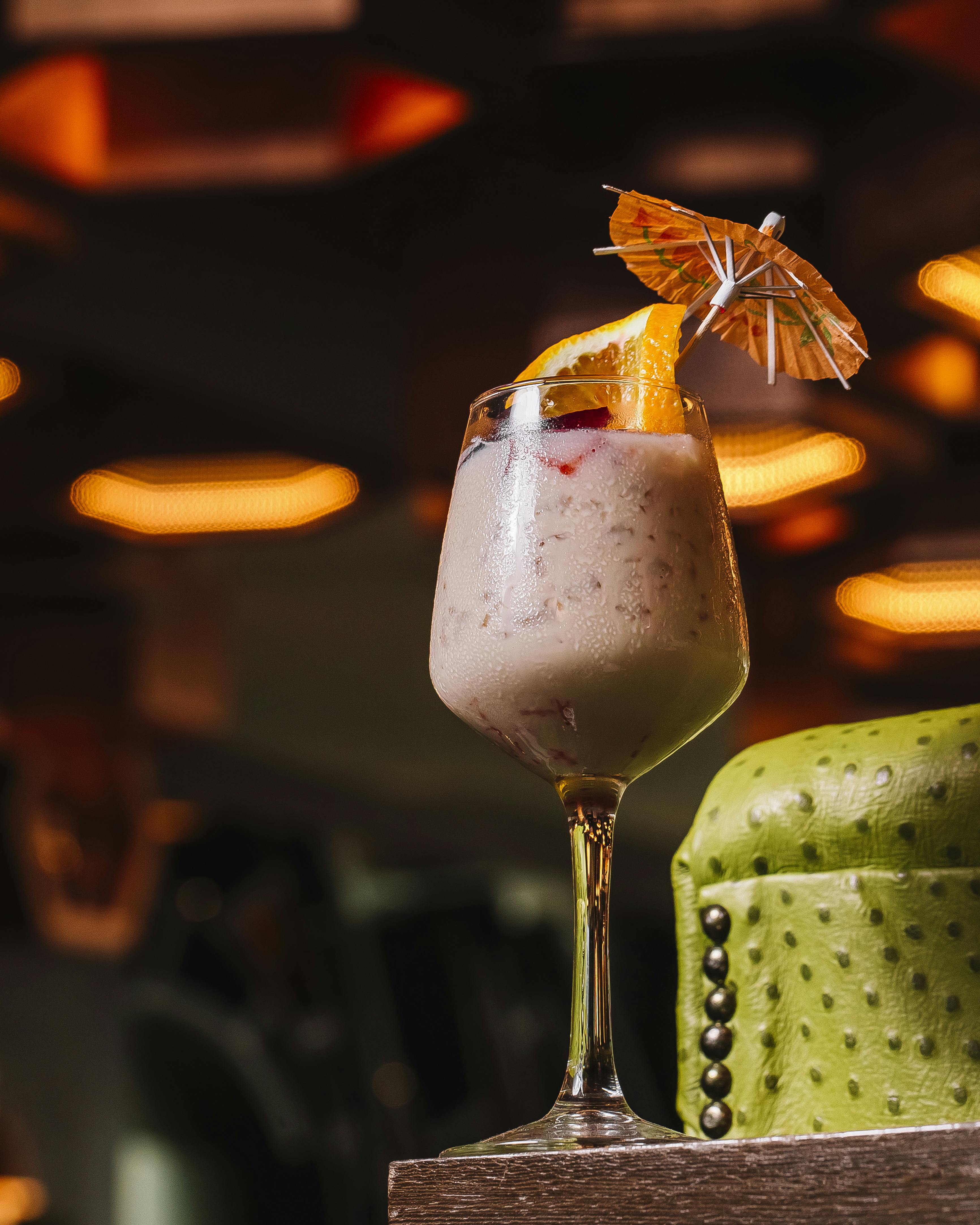A slushy cocktail in a glass, garnished with a slice of citrus and a small decorative umbrella.