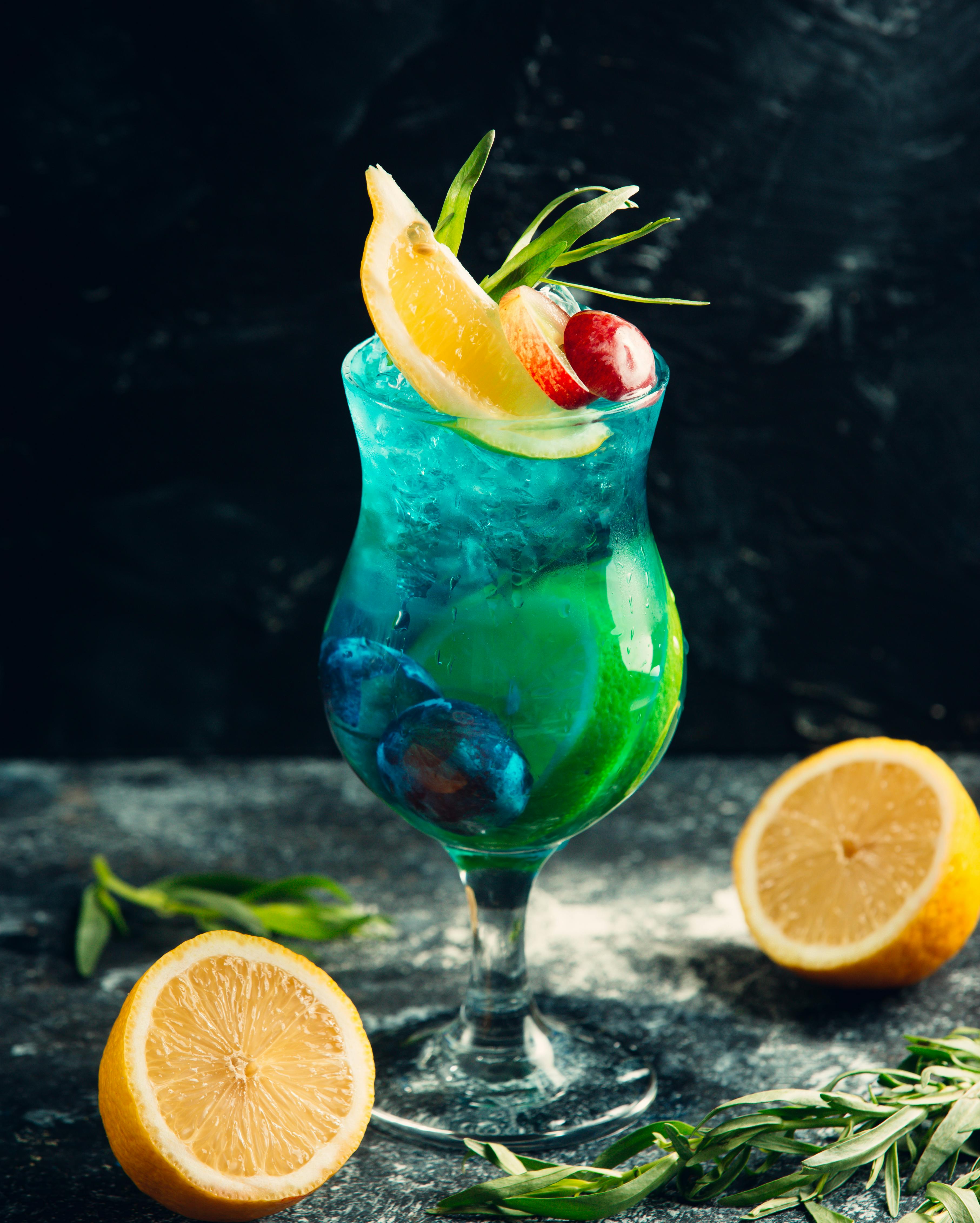 A glass of light blue cocktail, garnished with a variety of herbs and fruits.