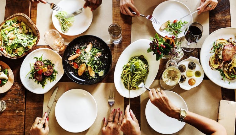 A table spread with different plates of food, with hands indicating people are eating.