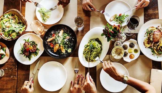 A table spread with different plates of food, with hands indicating people are eating.