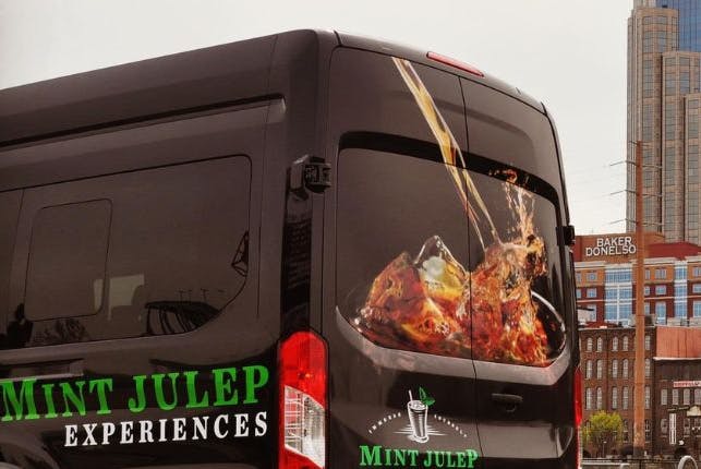 A Mint Julep Experiences luxury vehicle with Nashville's iconic buildings in the background.
