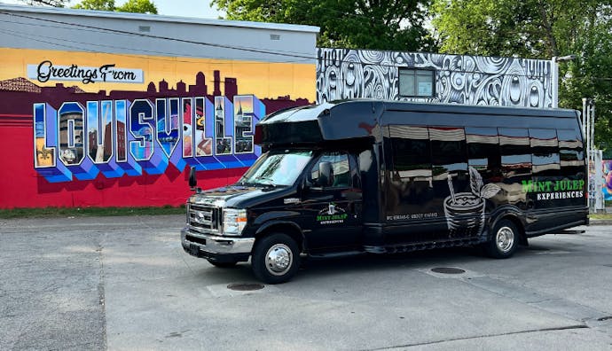 A Mint Julep Experiences luxury tour vehicle parked in front of a "Greetings from Louisville" wall mural.
