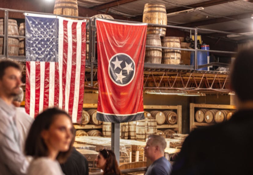 The interior of Pennington Distilling Co.'s rickhouse, with tourists exploring, while focusing on the USA and Tennessee flags displayed prominently.