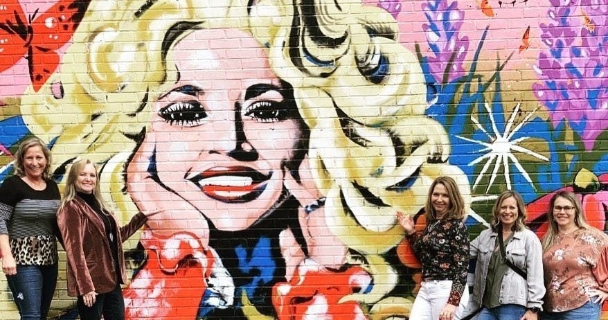 A group of tourists posing in front of a Nashville mural of Dolly Parton.