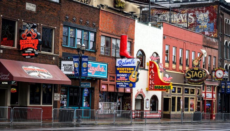 Bars and restaurants along Broadway in Nashville during the daytime, with storefronts and signs lining the street.