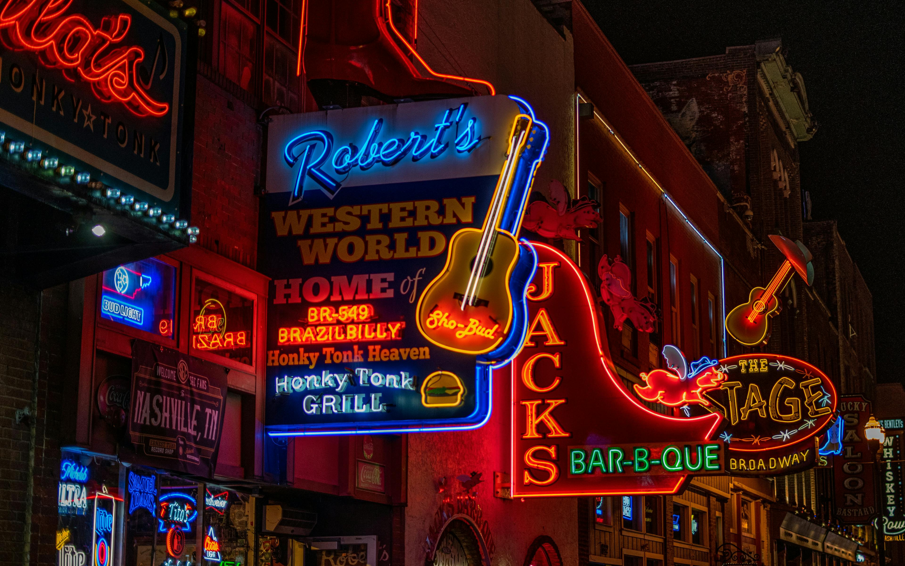 Nashville's Broadway street at night, illuminated by colorful neon signs from various establishments.
