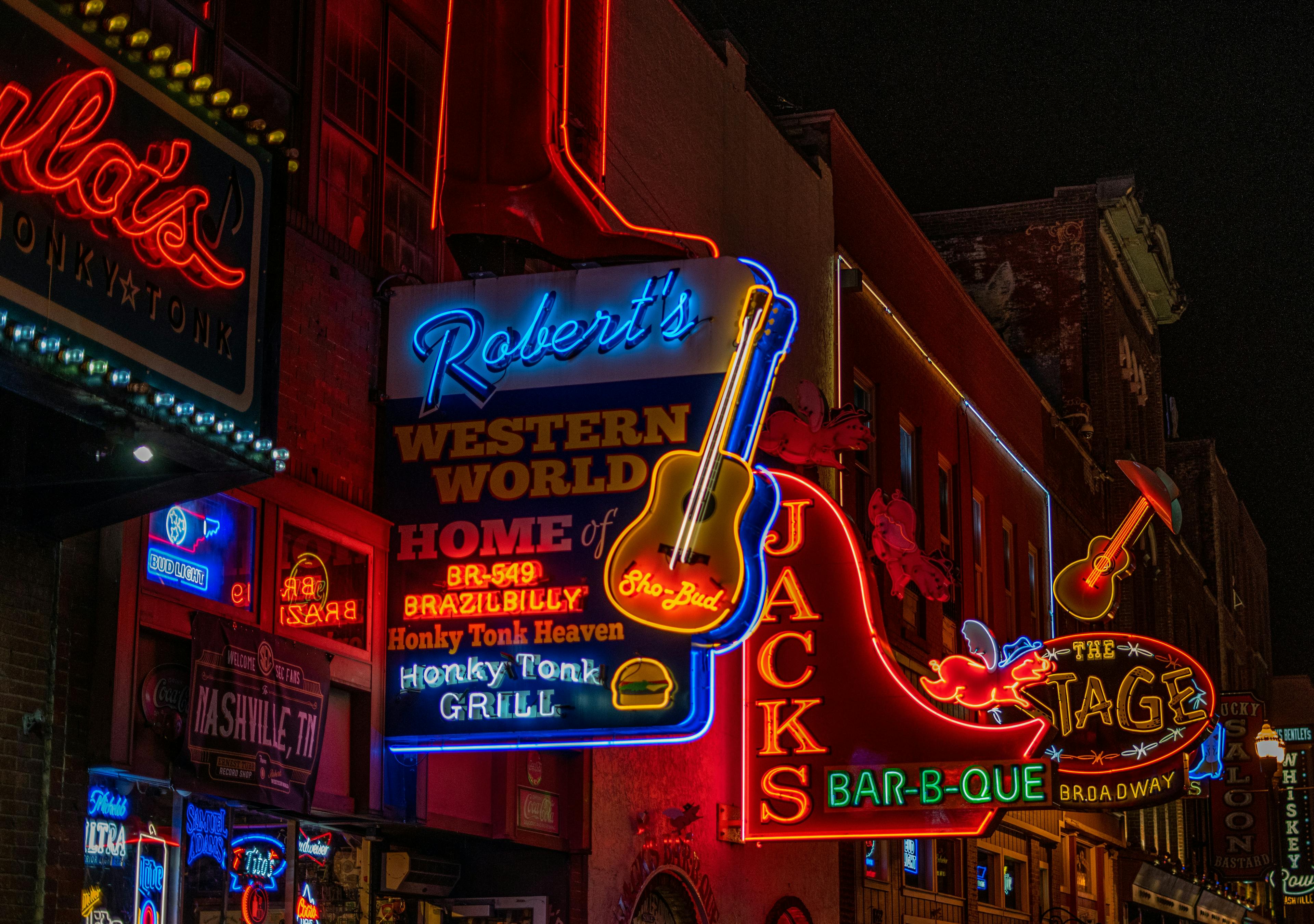Nashville's Broadway street at night, illuminated by vibrant neon signs from various establishments.