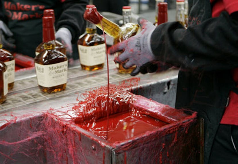 A gloved hand holding a Maker’s Mark bottle, preparing it for waxing during an interactive distillery tour experience.