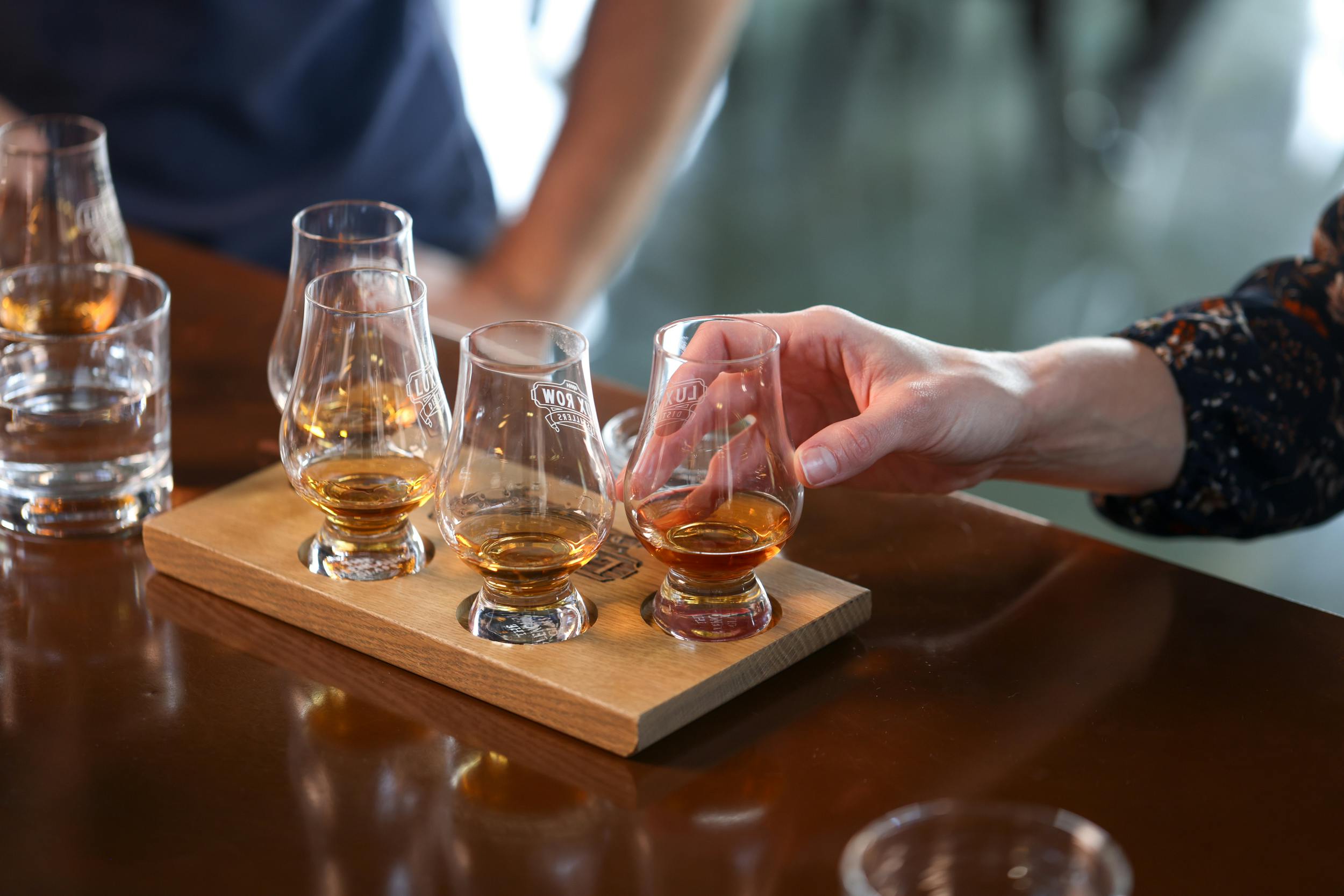 A set of glasses filled with bourbon samples, with a hand gently touching one.