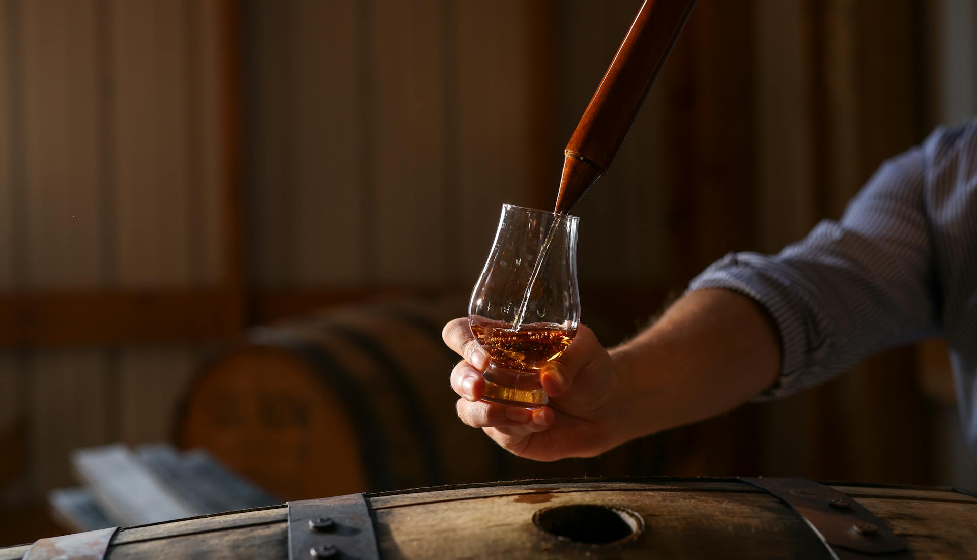 A hand holding a glass while bourbon is being poured into it.