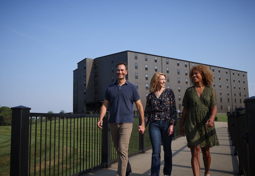 Two women and a man walk the grounds of a distillery with a bourbon barrel aging house in the background.