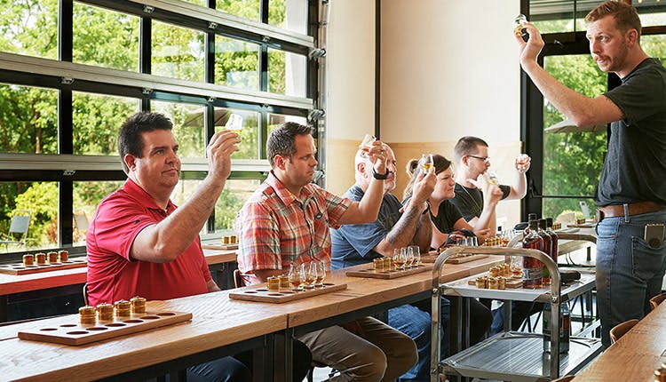 Tourists holding up and examining a glass of whiskey, with a guide in front of them.