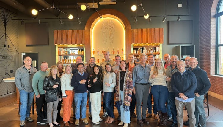 A large group of tourists posing inside Angel's Envy Distillery in Louisville, gathered together for a corporate event experience.