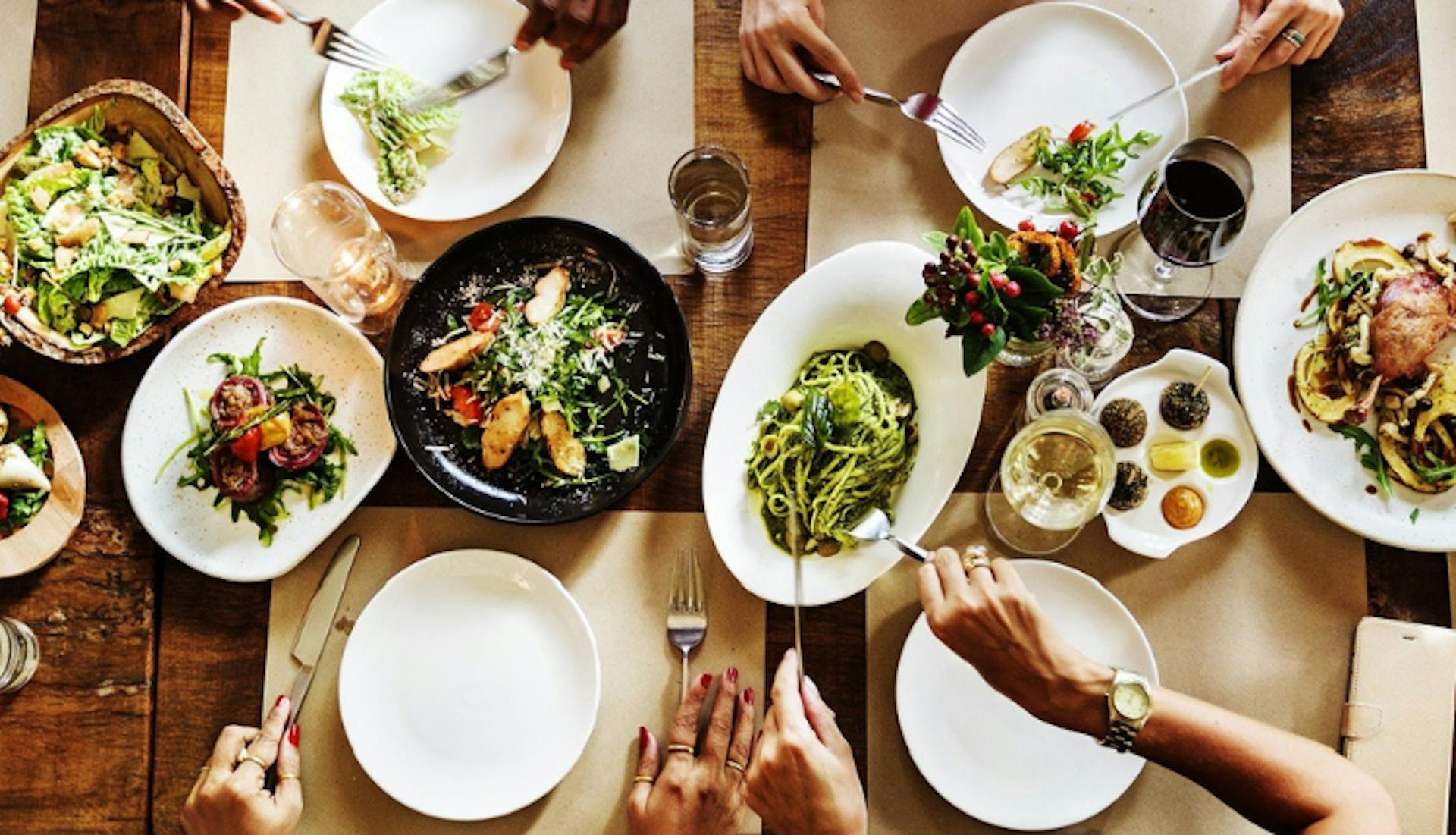 Hands reaching for dishes on a table filled with classic Louisville food, showcasing local flavors and shared dining.