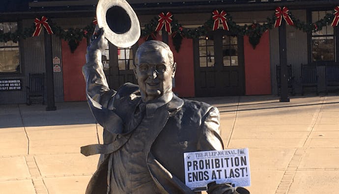 A statue of Jim Beam holding a 'Prohibition Ends At Last' paper, positioned in front of the American Stillhouse.