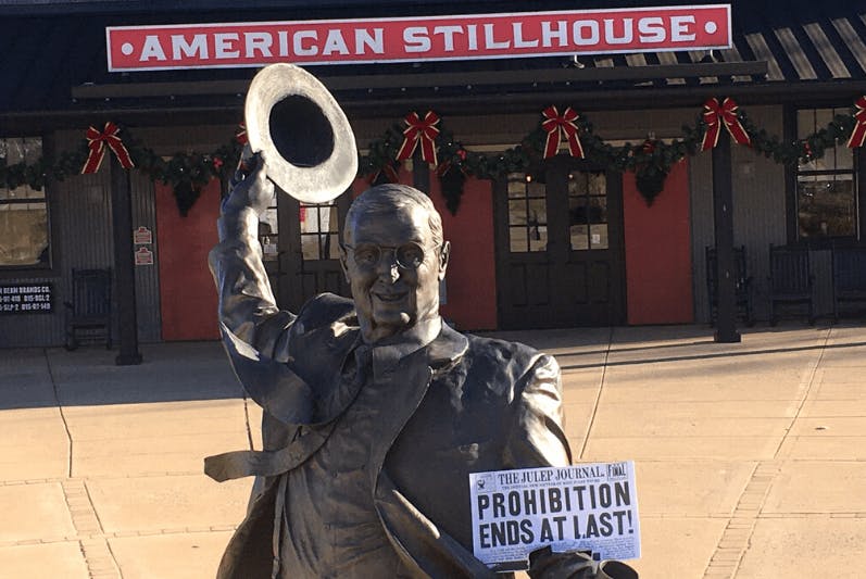 A statue of Jim Beam holding a 'Prohibition Ends At Last' paper, positioned in front of the American Stillhouse.