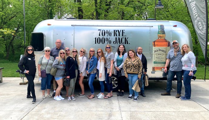 A group of tourists posing with a Jack Daniel's Airstream in the background on the distillery grounds.