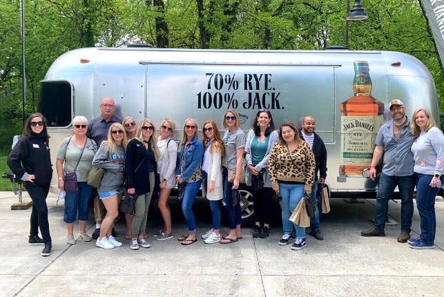 A group of tourists posing with a Jack Daniel's Airstream in the background on the distillery grounds.