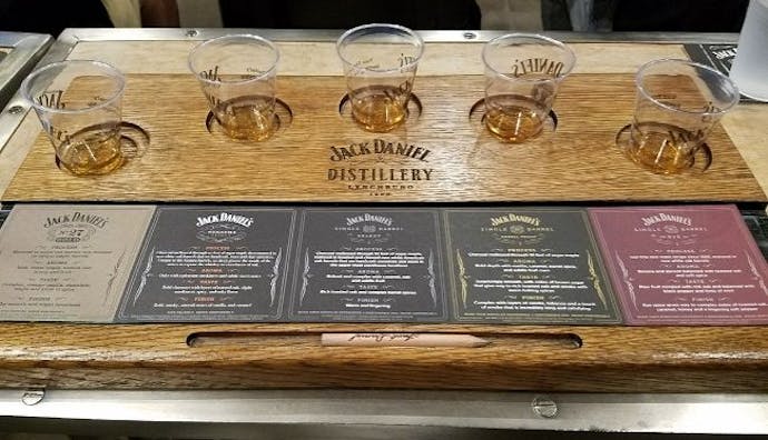 A set of drinking glasses with Jack Daniel's whiskey samples, accompanied by whiskey information cards on the table.