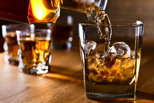 Bourbon being poured into a glass, with other glasses filled with bourbon slightly out of focus in the background.