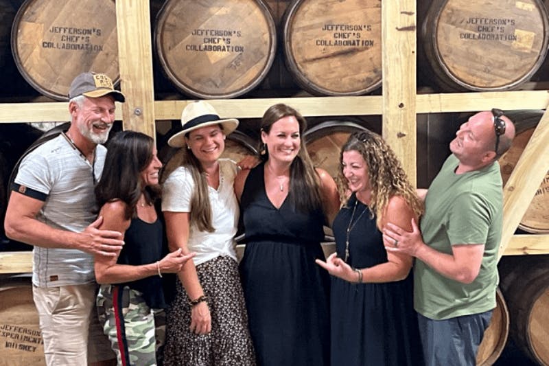 A group of tourists happily posing for a photo in front of a stack of barrels.