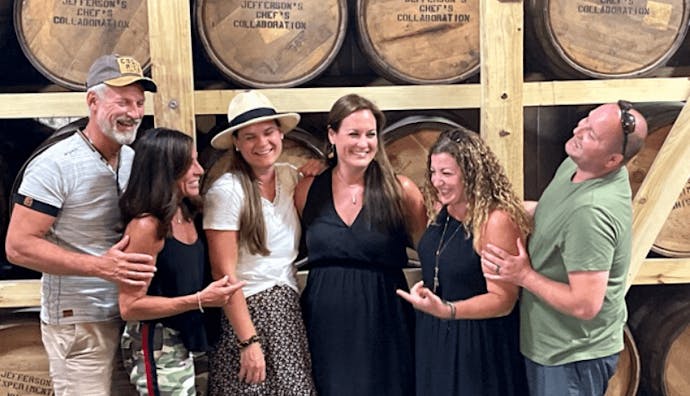 Tourists happily posing for photos, with a stack of wooden barrels in the background.