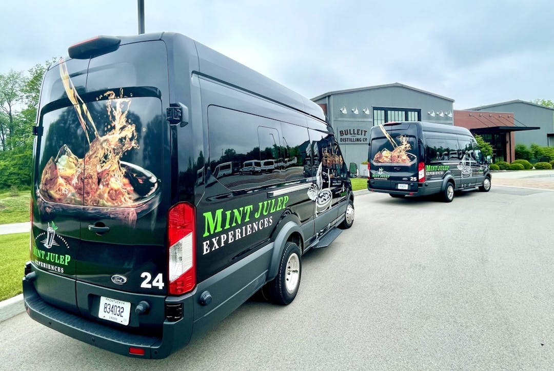 Two Mint Julep Experiences buses outside a Kentucky whiskey distillery. 