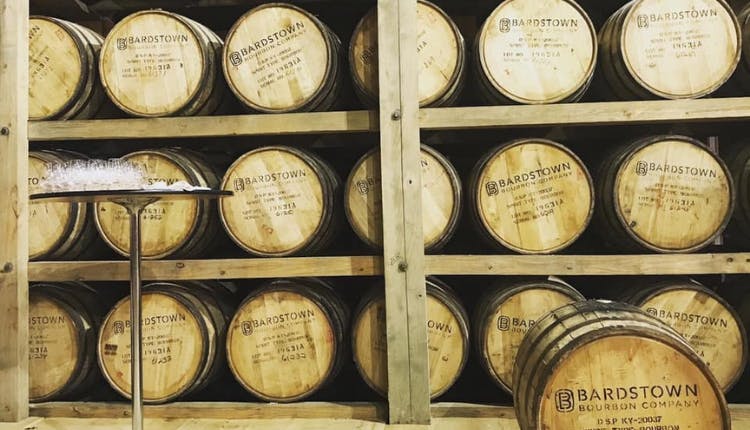 Wooden bourbon barrels from Bardstown Bourbon Company stacked in a warehouse.