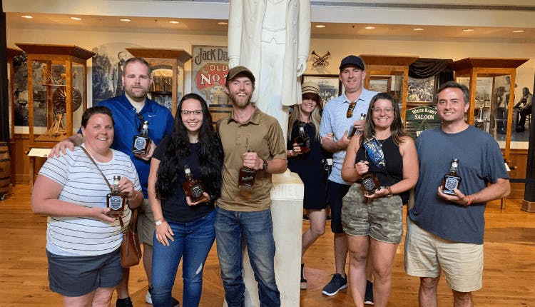 A group of tourists inside Jack Daniel's Distillery, each holding a bottle of whiskey and smiling for the photo.
