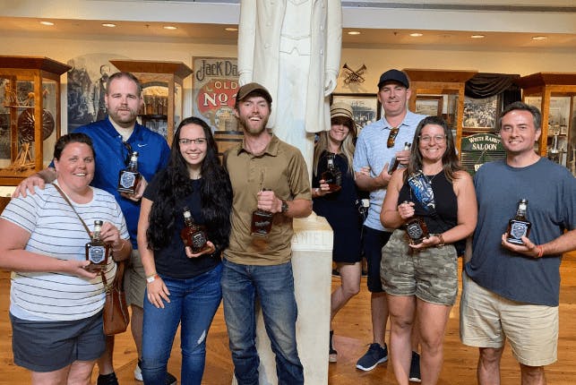 A group of tourists inside Jack Daniel's Distillery, each holding a bottle of whiskey and smiling for the photo.
