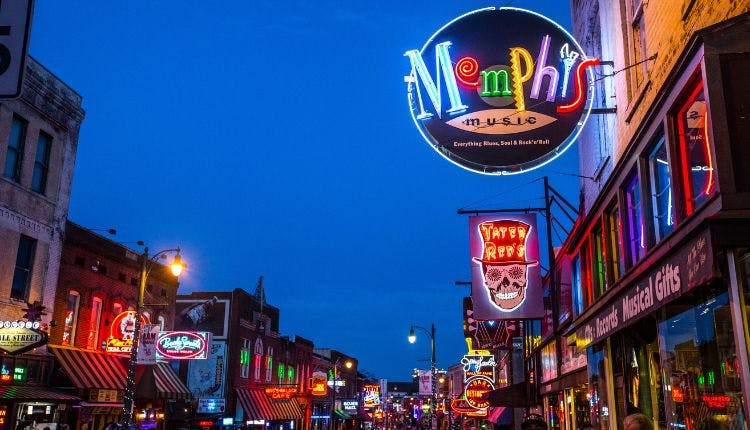 A view of Beale Street in Memphis at night, illuminated by bright neon lights from various establishments.