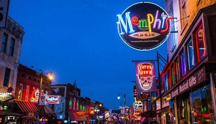 A view of Beale Street in Memphis at night, illuminated by bright neon lights from various establishments.
