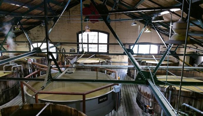 An interior view of an industrial distillery, showcasing large stills in the production area.
