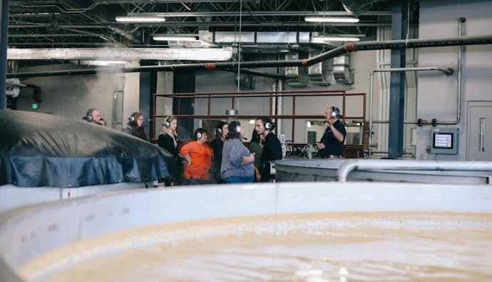 Tourists exploring an industrial distillery, with a guide speaking to them.