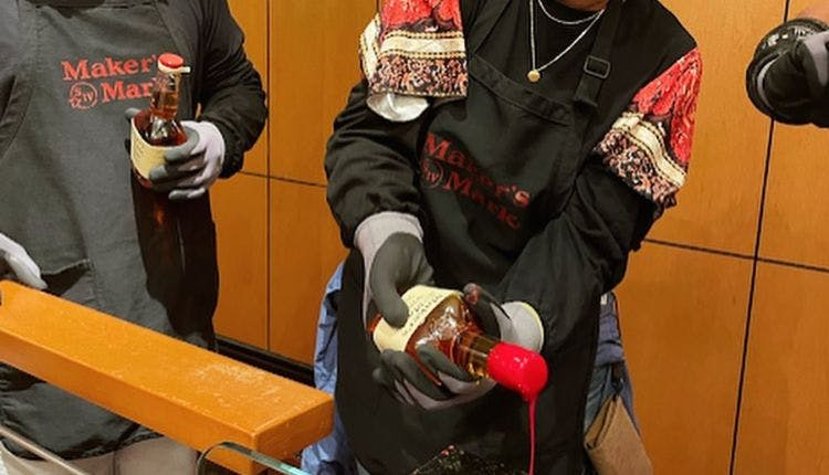 As part of the Maker’s Mark tour, a gloved hand carefully holds a bottle, getting it ready for the signature red wax dip.