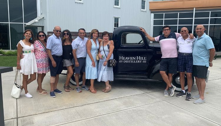 Tourists posing beside a vintage vehicle with the Heaven Hill Distillery logo.