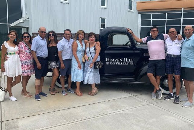 Tourists posing beside a vintage vehicle with the Heaven Hill Distillery logo.