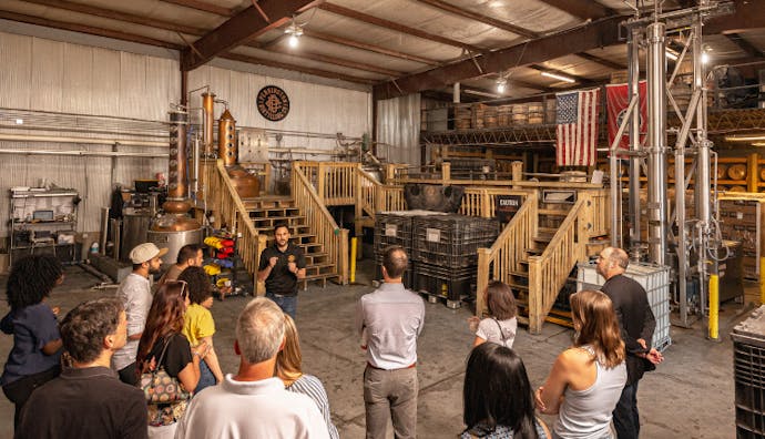 Tourists inside Pennington Distilling Co., standing and listening attentively as the guide speaks.