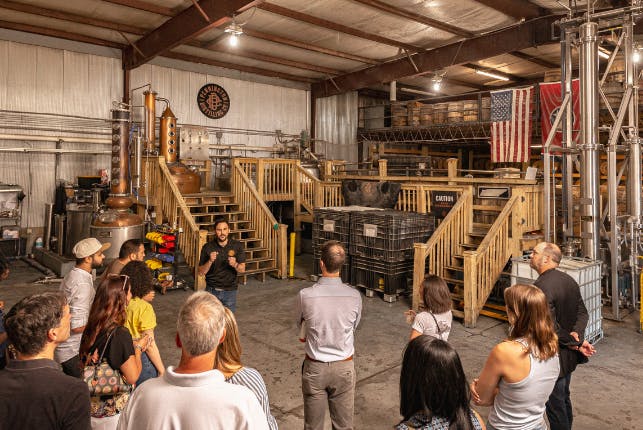 Tourists inside Pennington Distilling Co., standing and listening attentively as the guide speaks.