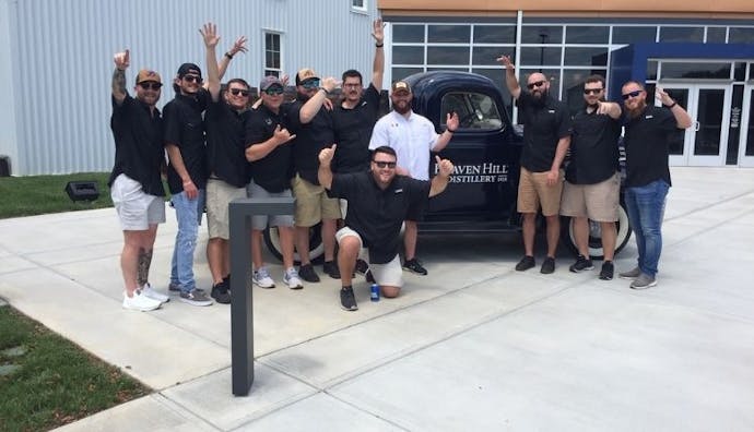 A group of tourists happily posing in front of a display vehicle with a Heaven Hill Distillery logo.