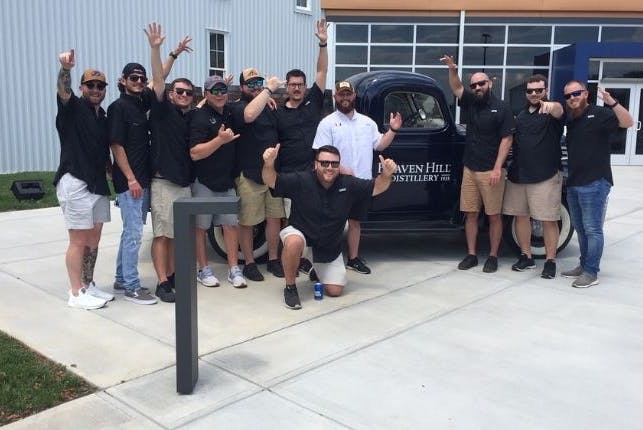 A group of tourists happily posing in front of a display vehicle with a Heaven Hill Distillery logo.