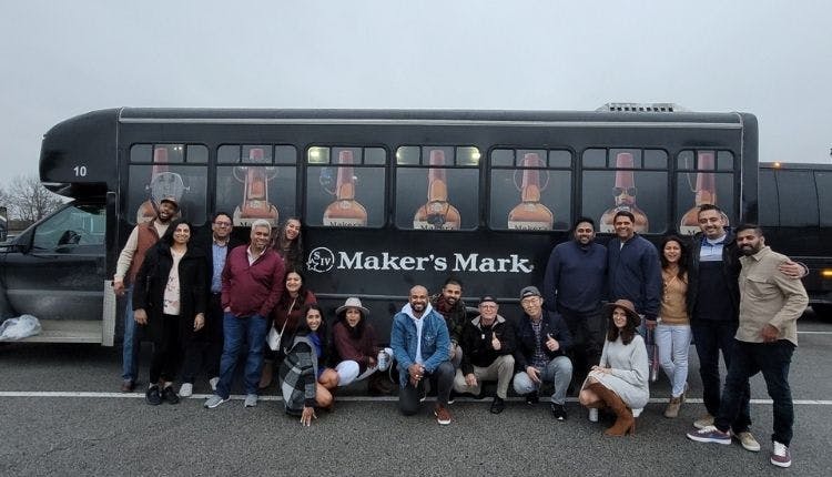A group of tourists happily posing in front of a Maker’s Mark tour bus, capturing a fun moment during their distillery visit.