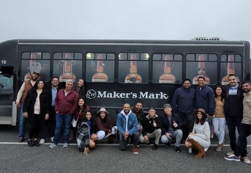 A group of tourists happily posing in front of a Maker’s Mark tour bus, capturing a fun moment during their distillery visit.