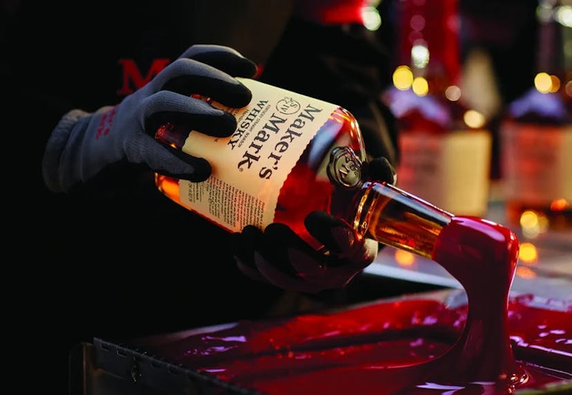 A gloved hand dipping a Maker's Mark bottle into red wax.