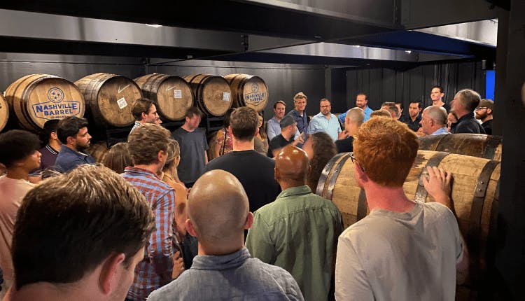 A group of people inside a barrel storage room during a Tennessee whiskey tour, attentively listening to the guide.