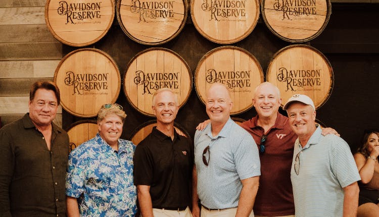 A group of tourists posing in front of a stack of Davidson Reserve wooden barrels.