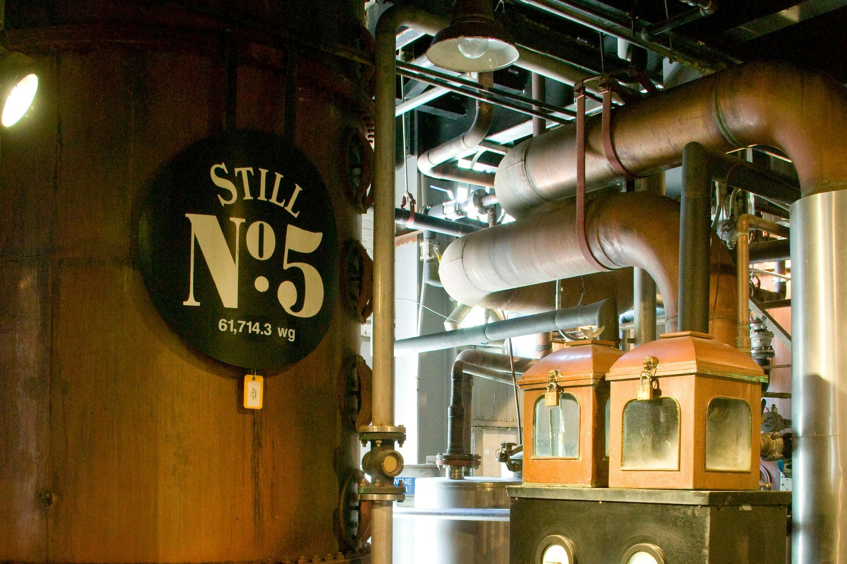 Interior of Jack Daniel's Distillery featuring "Still No. 5," a large copper still and a vintage control panel with gauges.